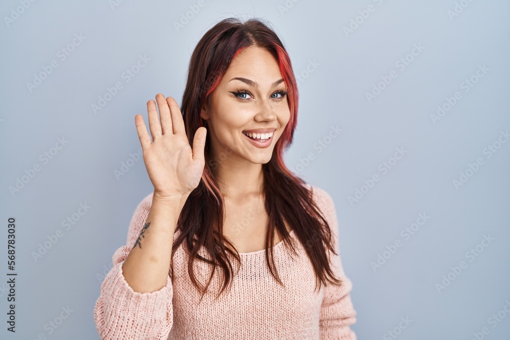 Young caucasian woman wearing pink sweater over isolated background waiving saying hello happy and smiling, friendly welcome gesture Young caucasian woman wearing pink sweater over isolated background waiving saying hello happy and smiling, friendly welcome gesture