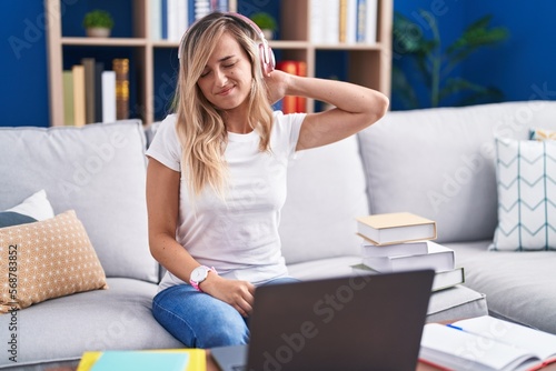 Young blonde woman studying using computer laptop at home suffering of neck ache injury, touching neck with hand, muscular pain