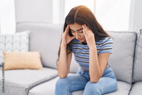 Young hispanic girl stressed sitting on sofa at home