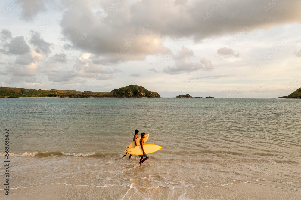 Indonesia, Lombok, Side view of surfers walking in sea at sunset