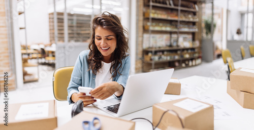 Quadro su tela Smiling online store owner reading a text message on her smartphone