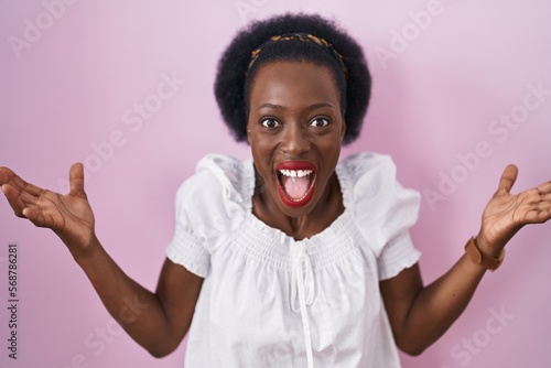 African woman with curly hair standing over pink background celebrating crazy and amazed for success with arms raised and open eyes screaming excited. winner concept