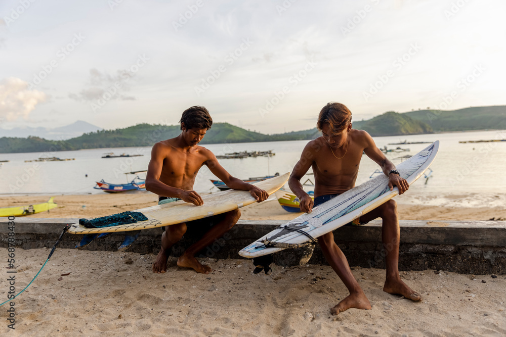 Indonesia, Lombok, Surfers preparing surfboards on beach at sunset