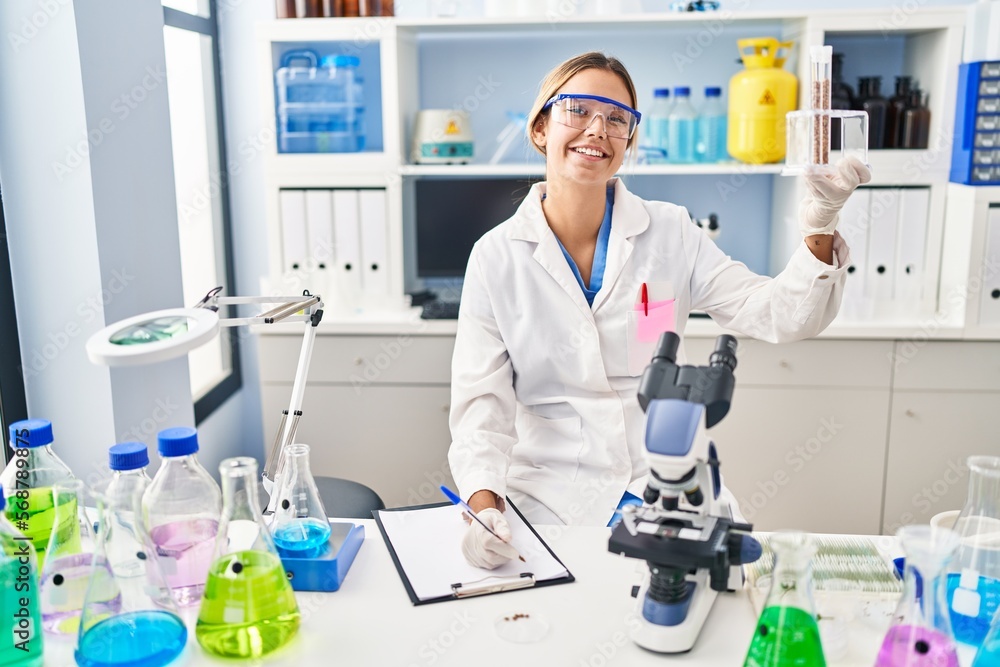 Young hispanic woman scientist write on document holding test tubes at laboratory Young hispanic woman scientist write on document holding test tubes at laboratory
