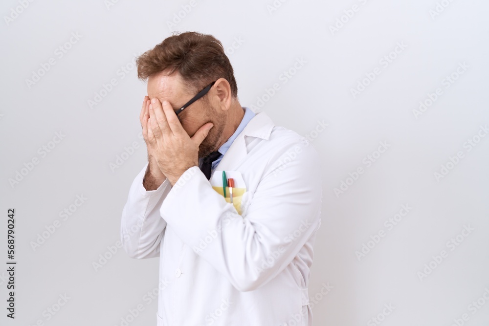 Middle age doctor man with beard wearing white coat with sad expression covering face with hands while crying. depression concept. Middle age doctor man with beard wearing white coat with sad expression covering face with hands while crying. depression concept.