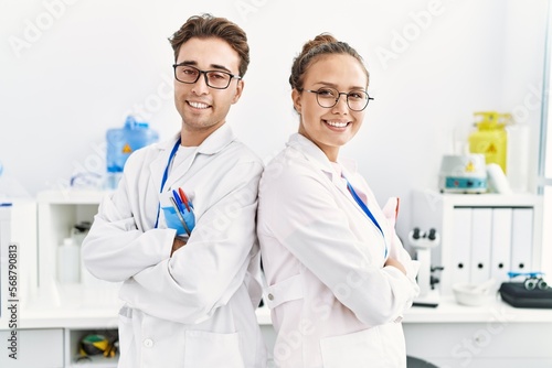 Man and woman wearing scientist uniform standing with arms crossed gesture at laboratory