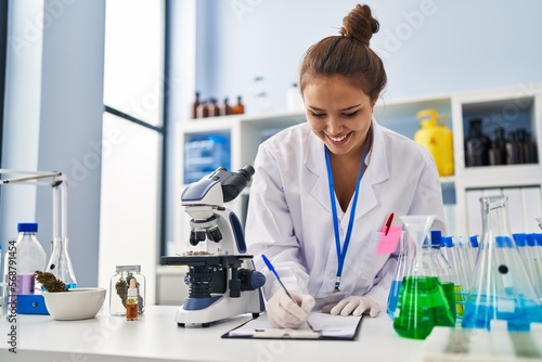 Young beautiful hispanic woman scientist smiling confident writing report working at laboratory