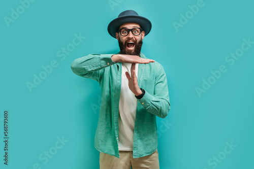 Young bearded hipster guy showing time out tired from work. Indoor studio shot against a blue background. photo