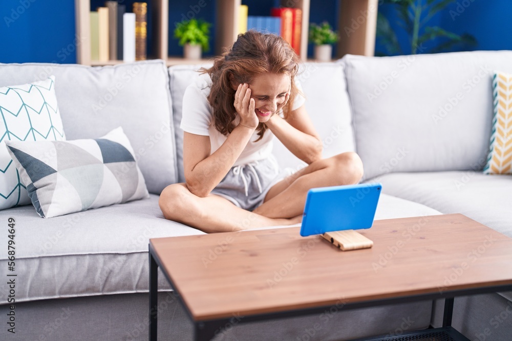 Young beautiful hispanic woman watching movie on touchpad sitting on sofa at home Young beautiful hispanic woman watching movie on touchpad sitting on sofa at home