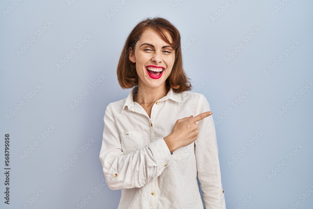 Young beautiful woman standing casual over blue background cheerful with a smile of face pointing with hand and finger up to the side with happy and natural expression on face Young beautiful woman standing casual over blue background cheerful with a smile of face pointing with hand and finger up to the side with happy and natural expression on face