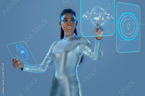 A model dressed as a robot wearing silver, futuristic  clothes holding a virtual  tablet, with virtual icons . A future technology concept photo