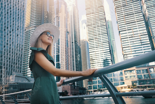 woman in fashionable summer dress and hat enjoying Dubai marina views with skyscrapers in United Arab Emirates