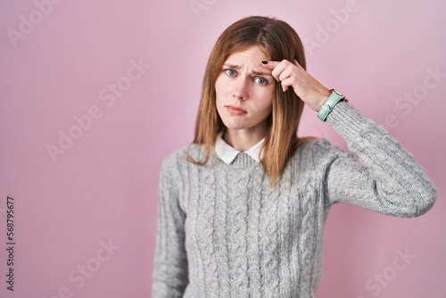 Beautiful woman standing over pink background pointing unhappy to pimple on forehead, ugly infection of blackhead. acne and skin problem