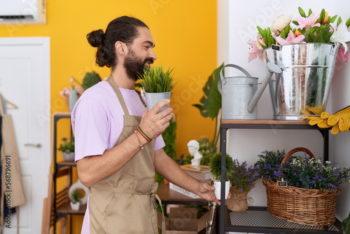 Young hispanic man florist putting plants on shelving at flower shop