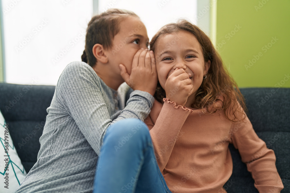 Two kids telling secret sitting on sofa at home Two kids telling secret sitting on sofa at home