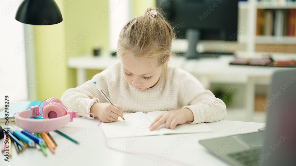 Adorable blonde girl student writing on notebook sitting on table at classroom Adorable blonde girl student writing on notebook sitting on table at classroom