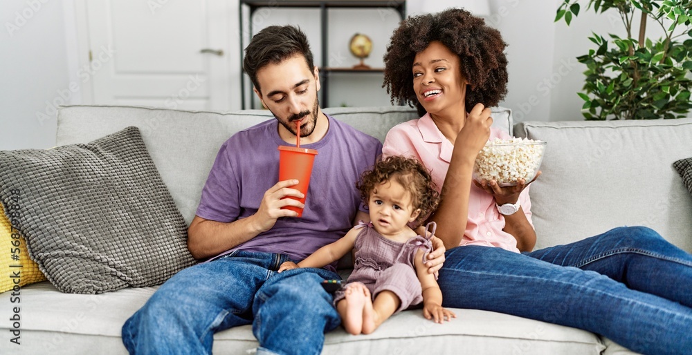 Couple and daughter watching movie sitting on sofa at home Couple and daughter watching movie sitting on sofa at home