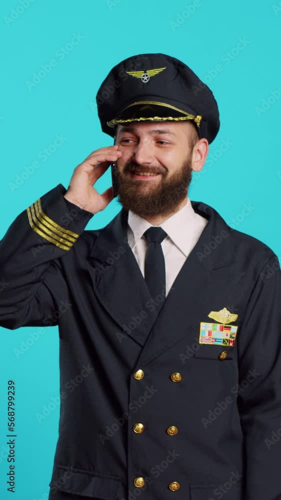 Vertical video: Male aviator talking on smartphone call and laughing, feeling positive and having remote conversation. Young cabin pilot wearing flying uniform for commercial flights, telephone line. Vertical video: Male aviator talking on smartphone call and laughing, feeling positive and having remote conversation. Young cabin pilot wearing flying uniform for commercial flights, telephone line.
