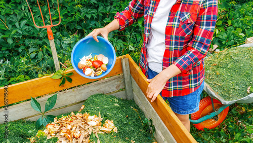 Kitchen waste, lawn clippings as composting ingredients close up. A woman throws food waste into a wooden compost bin. Maintaining organic farming on the principle of zero waste concept.