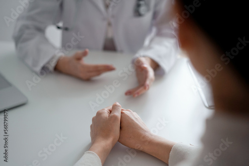 Doctor and patient discussing current health examination while sitting at the desk in clinic office. The focus is on female patient's hands, close up. Medicine concept