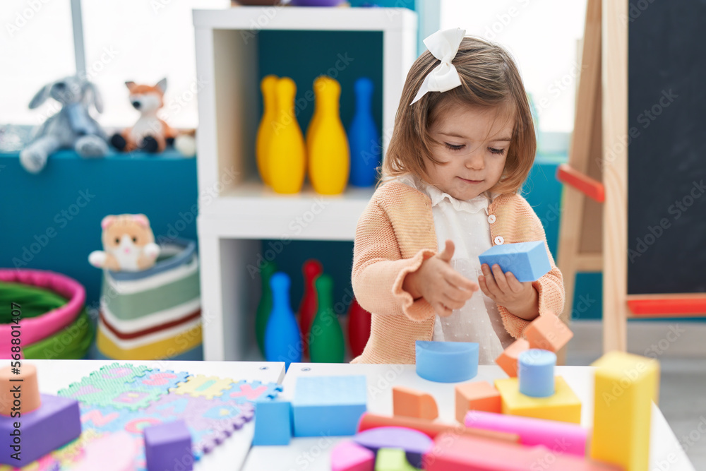Adorable blonde toddler playing with construction blocks standing at kindergarten Adorable blonde toddler playing with construction blocks standing at kindergarten