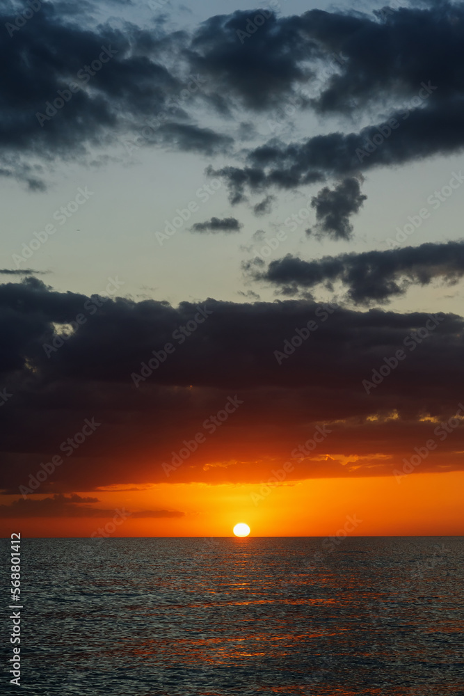 Horizontal photo of the sunset over the sea. Clouds in the sky in the evening, bright sun.