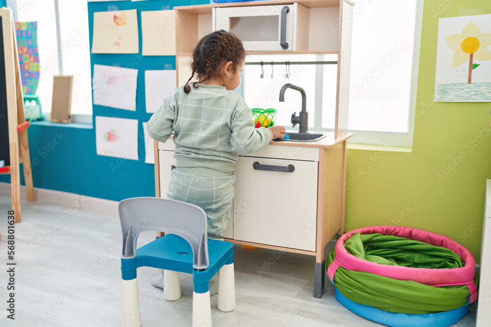 Adorable hispanic toddler playing with play kitchen standing at kindergarten Adorable hispanic toddler playing with play kitchen standing at kindergarten