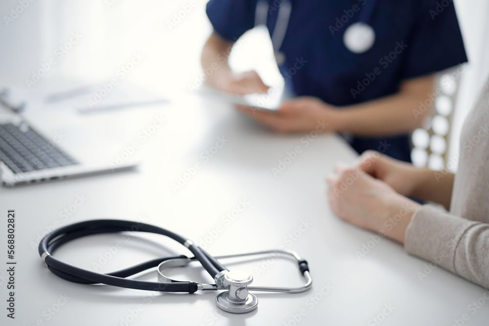 Stethoscope lying on the tablet computer in front of a doctor and patient at the background. Medicine, healthcare concept Stethoscope lying on the tablet computer in front of a doctor and patient at the background. Medicine, healthcare concept