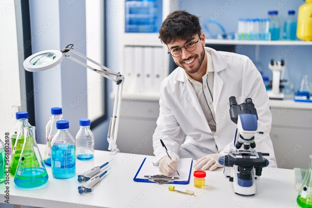 Young hispanic man scientist writing on document holding urine test tube at laboratory Young hispanic man scientist writing on document holding urine test tube at laboratory