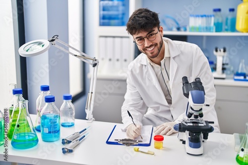 Valokuvatapetti Young hispanic man scientist writing on document holding urine test tube at labo