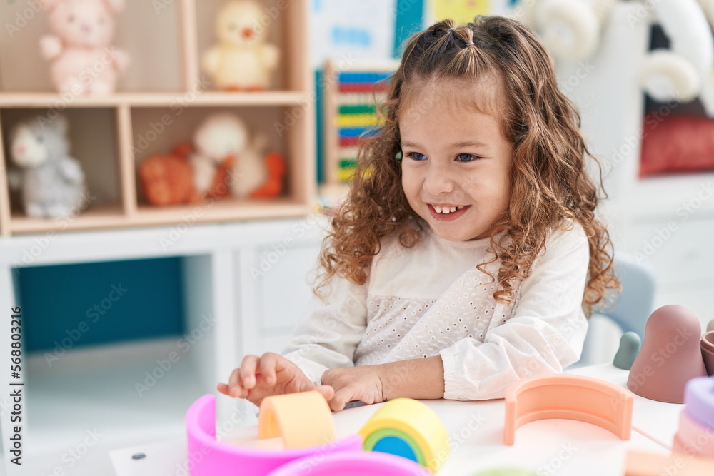 Fototapeta premium Adorable blonde toddler playing with toys sitting on table at kindergarten