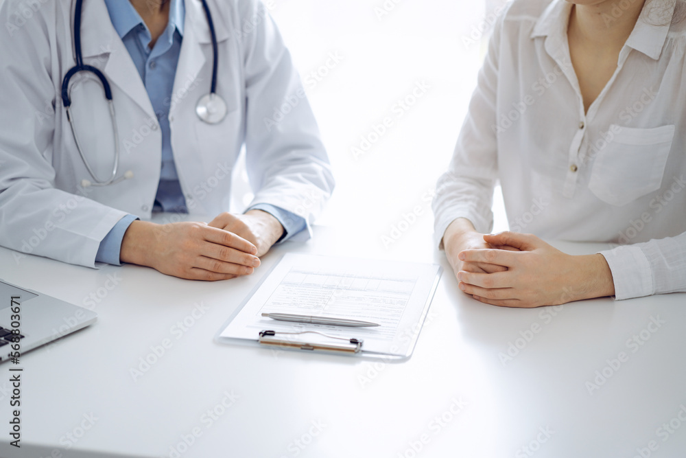 Doctor and patient discussing current health questions while sitting near of each other and using clipboard at the table in clinic, just hands closeup. Medicine concept Doctor and patient discussing current health questions while sitting near of each other and using clipboard at the table in clinic, just hands closeup. Medicine concept