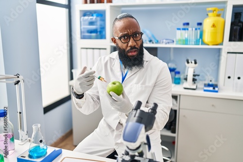 African american man working at scientist laboratory with apple in shock face  looking skeptical and sarcastic  surprised with open mouth