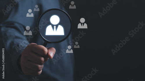 Businessman holding magnifying glass with virtual graphic human icon for human development recruitment leadership and customer target group concept. HRM or Human Resource Management. Hr concept.