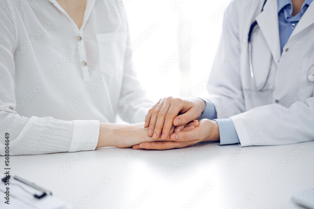 Doctor and patient sitting near each other at the table in clinic office. The focus is on female physician's hands reassuring woman, only hands, close up. Medicine concept Doctor and patient sitting near each other at the table in clinic office. The focus is on female physician's hands reassuring woman, only hands, close up. Medicine concept