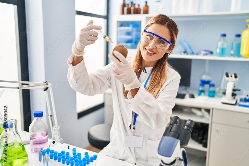 Young blonde woman wearing scientist uniform injecting on kiwi at laboratory Young blonde woman wearing scientist uniform injecting on kiwi at laboratory