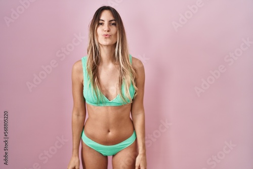 Young hispanic woman wearing bikini over pink background looking at the camera blowing a kiss on air being lovely and sexy. love expression.