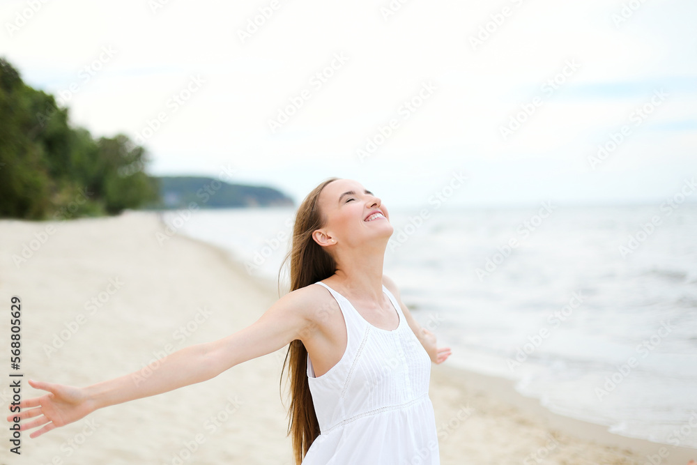 Happy smiling woman in free happiness bliss on ocean beach standing with open hands. Portrait of a multicultural female model in white summer dress enjoying nature during travel holidays vacation Happy smiling woman in free happiness bliss on ocean beach standing with open hands. Portrait of a multicultural female model in white summer dress enjoying nature during travel holidays vacation