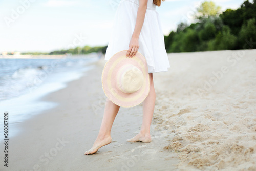 Young woman on a beach holding a white hat. Legs close up