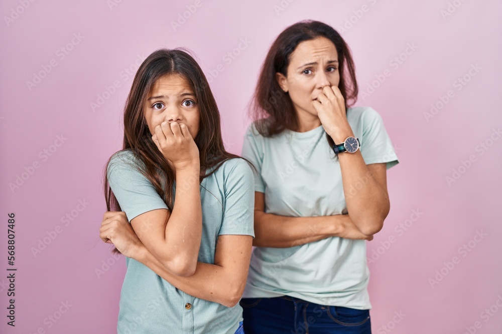 Young mother and daughter standing over pink background looking stressed and nervous with hands on mouth biting nails. anxiety problem. Young mother and daughter standing over pink background looking stressed and nervous with hands on mouth biting nails. anxiety problem.