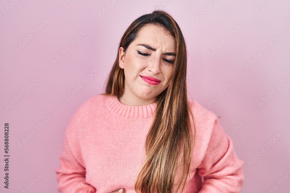 Young hispanic woman standing over pink background with hand on stomach because indigestion, painful illness feeling unwell. ache concept. Young hispanic woman standing over pink background with hand on stomach because indigestion, painful illness feeling unwell. ache concept.