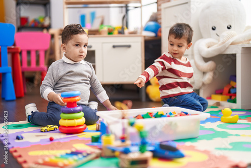 Two kids playing with toys sitting on floor at kindergarten