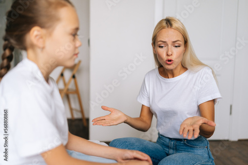 Closeup side view of furious emotional young blonde mom scolding, raising voice, scream and gesturing with hands at stubborn difficult little child daughter at home. Concept of mother-children problem