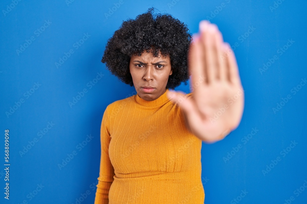 Black woman with curly hair standing over blue background doing stop sing with palm of the hand. warning expression with negative and serious gesture on the face. Black woman with curly hair standing over blue background doing stop sing with palm of the hand. warning expression with negative and serious gesture on the face.