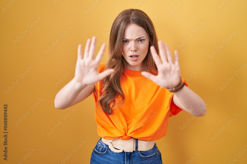 Caucasian woman standing over yellow background doing stop gesture with hands palms, angry and frustration expression Caucasian woman standing over yellow background doing stop gesture with hands palms, angry and frustration expression