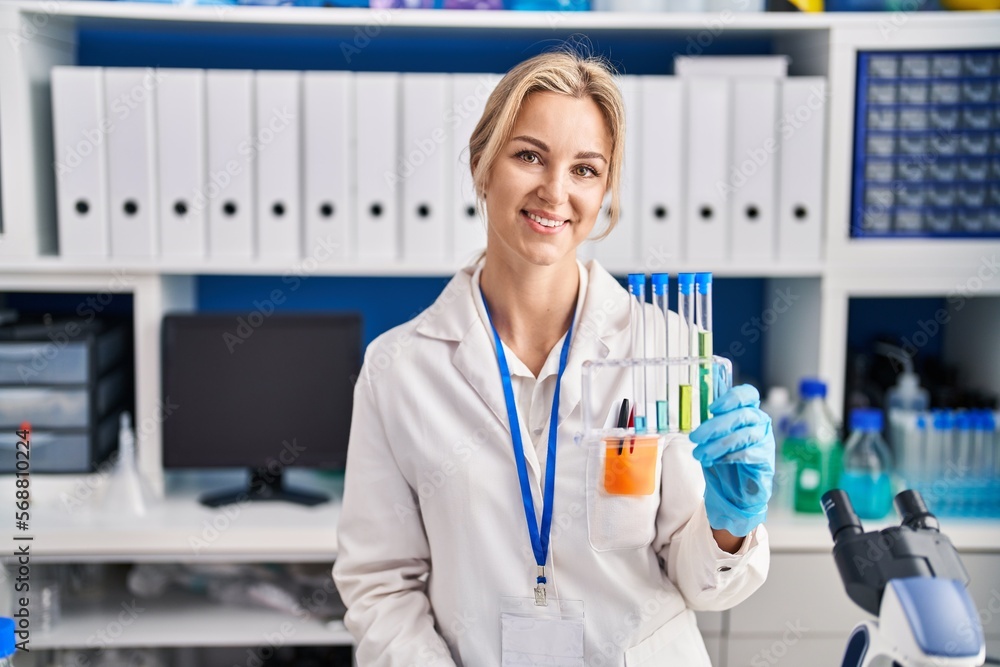 Young caucasian woman working at scientist laboratory holding test tubes looking positive and happy standing and smiling with a confident smile showing teeth Young caucasian woman working at scientist laboratory holding test tubes looking positive and happy standing and smiling with a confident smile showing teeth