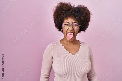 Young african american woman standing over pink background sticking tongue out happy with funny expression. emotion concept.