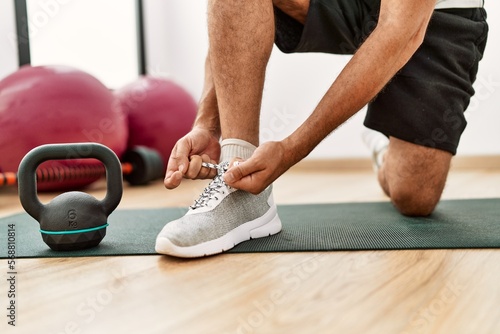 Middle age grey-haired man tying shoe at sport center