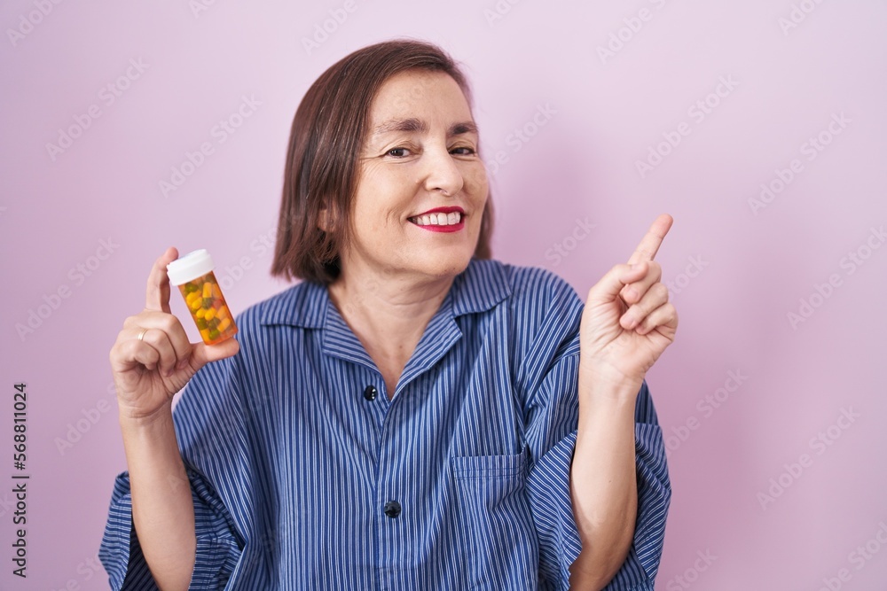 Middle age hispanic woman holding pills smiling happy pointing with hand and finger to the side Middle age hispanic woman holding pills smiling happy pointing with hand and finger to the side