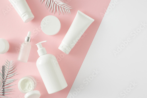 Summer skincare concept. Top view photo of cosmetic tubes, dropper bottle, pump bottle and tropical leaves on pastel pink and white background with empty space. Flat lay cosmetics mockup idea.